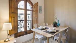 Un'area pranzo con un tavolo apparecchiato per due, una lampada e vista su un balcone attraverso una porta in legno.