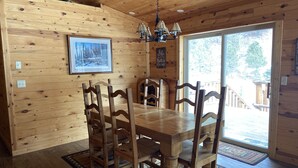 Une salle à manger en bois, avec une grande table et des chaises, un lustre et un tableau encadré au mur.