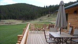 Une terrasse en bois avec des sièges et une table, donnant sur une zone herbeuse et des collines boisées.