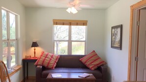 A living room with a brown leather sofa, two striped pillows, a wooden coffee table, a lamp, and a ceiling fan. - Mimi's Mansion At Stacy Ranch, Cabin On 120 Acres Between Ingram & Hunt, Tx (Ingram)