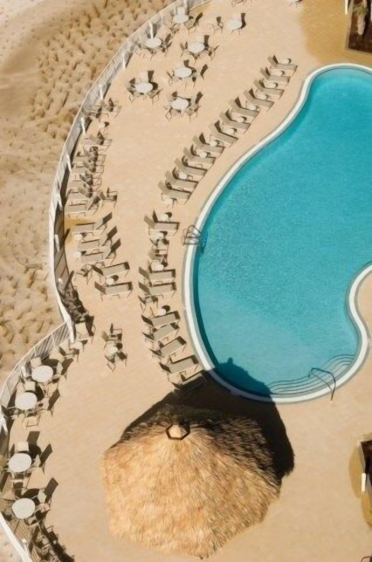 Un área junto a la piscina con sillones de descanso y una sombrilla de paja.