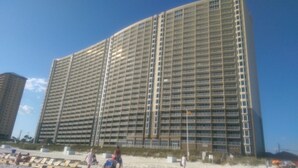 Ein Hochhaus-Hotel mit mehreren Etagen und Balkonen, nahe am Strand, mit einigen Personen im Vordergrund.