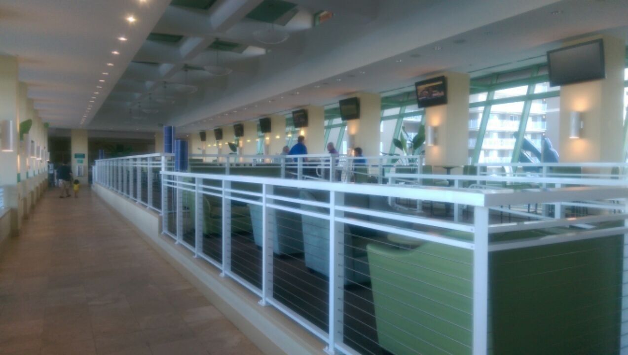 A long corridor with a white railing, green seating areas, and a tiled floor.