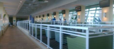 A long corridor with a white railing, green seating areas, and a tiled floor.