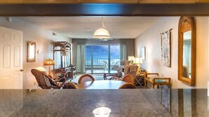 Hotelkamer met een eethoek, een groot raam met uitzicht, een kroonluchter en een spiegel aan de muur.