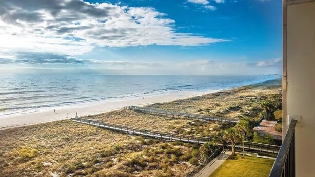 Uitzicht op de kust met een strand, een houten looppad en een heldere lucht.