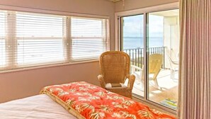 Een slaapkamer met een bed, een rieten stoel en een balkon met zitplaatsen.