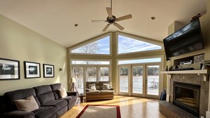 A spacious living room with a large window, a fireplace, and a ceiling fan. - Lake Escape - Unobstructed Views at our Group-Friendly Retreat! (Bracey)
