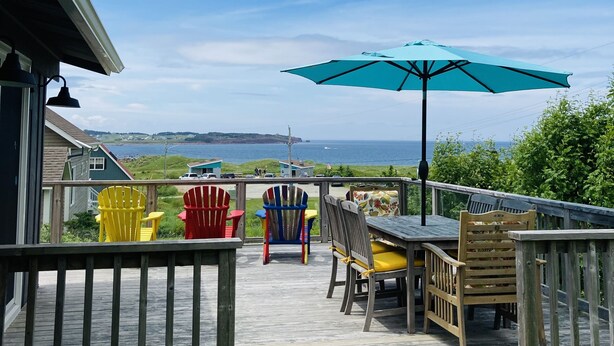 Une terrasse en bois, aménagée avec du mobilier d’extérieur, notamment des chaises et une table, et offrant une vue sur une étendue d’eau.