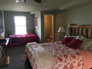 Ein Schlafzimmer mit zwei Betten, einem Schreibtisch, einem Stuhl, einer Lampe und einem Deckenventilator.