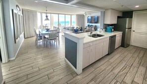 A modern kitchen with a central island, a dining area with a view, and a large window overlooking the ocean. - 3 BR/3BA Updated End Condo w/2 Balconies! Comp Beach Chairs/Umbrella Seasonal (Panama City Beach)