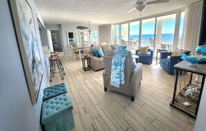 Uma sala de estar ampla com varanda vista para o mar, uma área de jantar e uma cozinha.