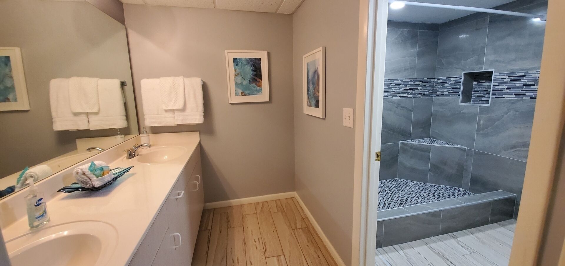 A modern bathroom with a large sink, mirror, and two framed artworks.