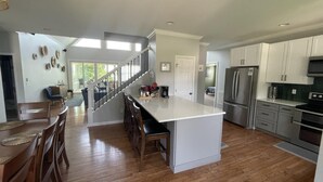 A spacious kitchen with a central island, stainless steel appliances, and a wooden dining area. - Beautiful large family home with dock on Lake Keowee! (Seneca)