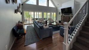 A spacious living room with a high ceiling, large windows, a fireplace, and a staircase. - Beautiful large family home with dock on Lake Keowee! (Seneca)