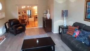 A spacious living room with a high ceiling, a dining area in the background, and a sofa with decorative pillows.