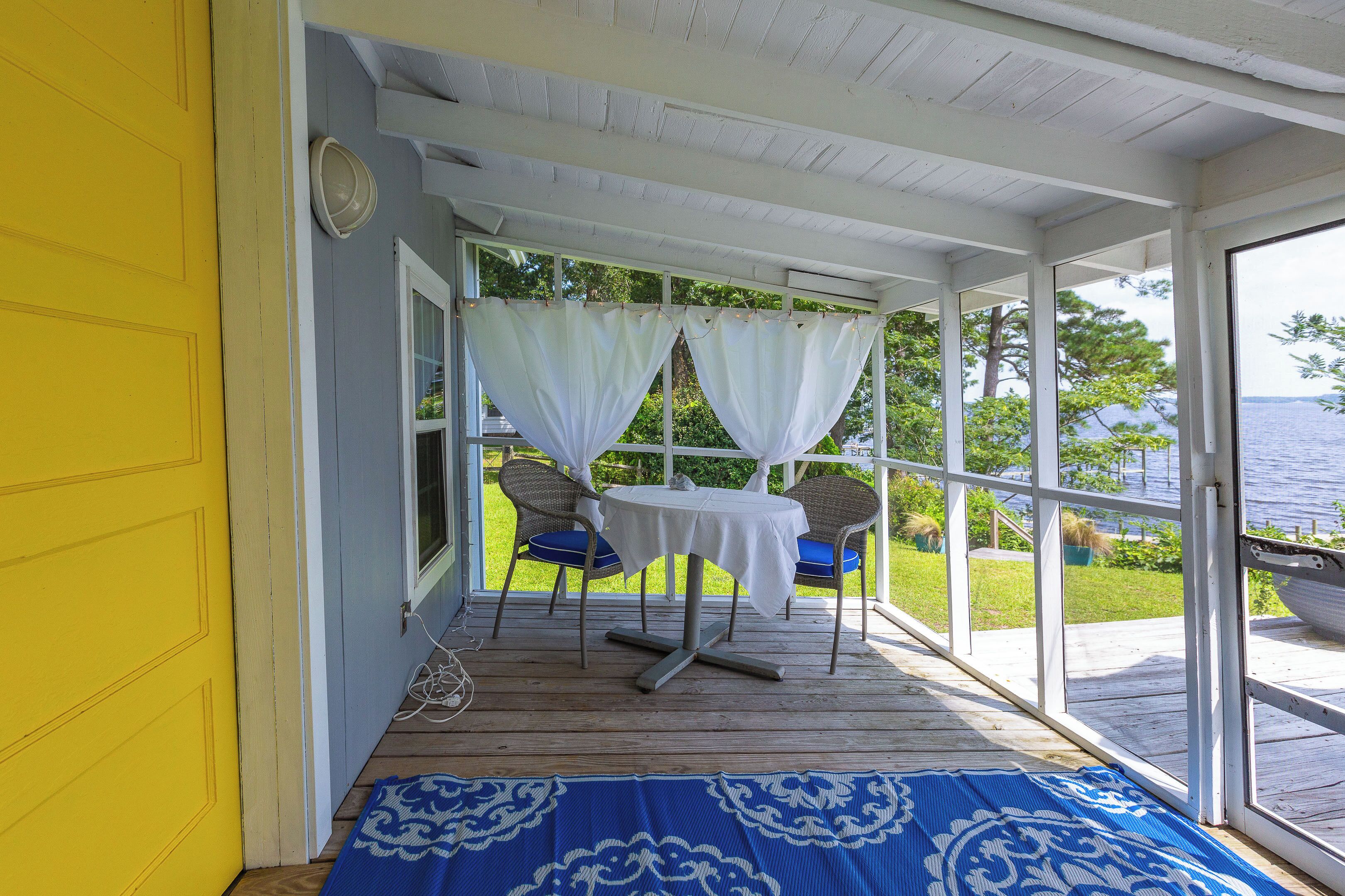 A covered porch with a table and chairs, a view of the outdoors, and a yellow door.