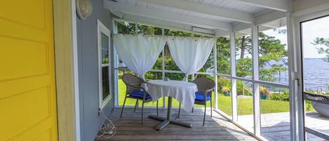 A covered porch with a table and chairs, a view of the outdoors, and a yellow door.