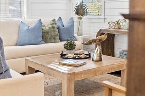 A cozy living room with a beige sofa, blue and green cushions, a wooden coffee table with a book and decorative items, and a rustic wall decor.