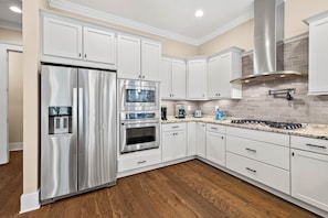 A modern kitchen with white cabinets, stainless steel appliances, and a tiled backsplash. - Golf Cart & 4 Bikes! Next to Huge Resort Pool! Sandy Curls Cottage Highland Parks (Santa Rosa Beach)