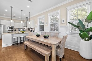 A modern kitchen with white cabinetry, a wooden dining table, and bar stools.