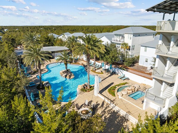 A resort with a large pool, multiple lounge areas, and a view of the surrounding forest.