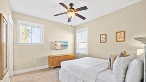 A bedroom with a bed, a ceiling fan, a dresser, and two windows. - Golf Cart & 4 Bikes! Next to Huge Resort Pool! Sandy Curls Cottage Highland Parks (Santa Rosa Beach)