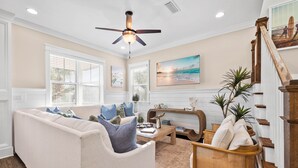A living room with a beige sofa, wooden coffee table, and a wooden chair. A ceiling fan is visible above.
