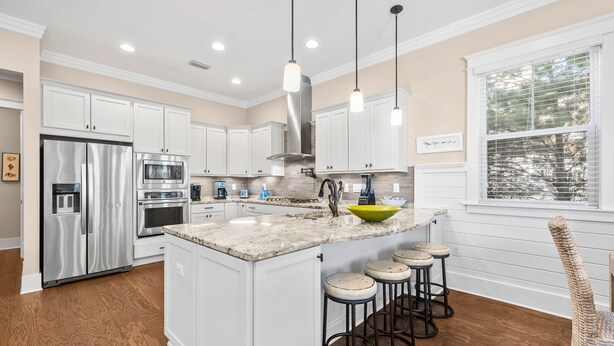 A modern kitchen with white cabinets, stainless steel appliances, a large island with stools, and pendant lighting. - Golf Cart & 4 Bikes! Next to Huge Resort Pool! Sandy Curls Cottage Highland Parks (Santa Rosa Beach)
