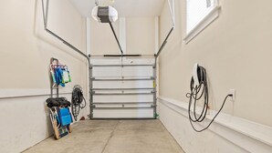 A clean, well-lit hallway with a closed garage door, a cart with luggage, and a power outlet on the wall. - Golf Cart & 4 Bikes! Next to Huge Resort Pool! Sandy Curls Cottage Highland Parks (Santa Rosa Beach)