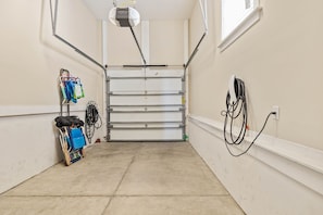 A clean, well-lit hallway with a closed garage door, a cart with luggage, and a power outlet on the wall. - Golf Cart & 4 Bikes! Next to Huge Resort Pool! Sandy Curls Cottage Highland Parks (Santa Rosa Beach)