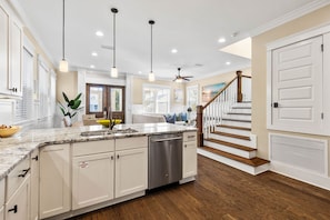 A spacious kitchen with a large island, white cabinetry, and a dishwasher. There is a staircase leading to a second floor with a wooden railing. - Golf Cart & 4 Bikes! Next to Huge Resort Pool! Sandy Curls Cottage Highland Parks (Santa Rosa Beach)
