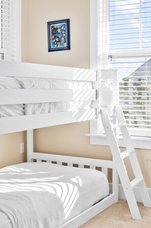 Una cama litera con escalera, un cuadro en la pared y una ventana con persianas.