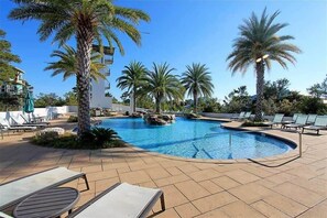 Un área de piscina con sillones de descanso y palmeras.