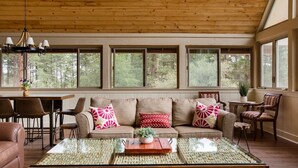 A cozy living room with a wooden ceiling, large windows, a sofa with patterned cushions, and a glass coffee table. - Spacious Prescott Forest Cabin, Game Room, 15 minutes to Downtown Prescott (Prescott)