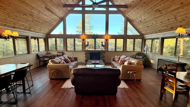 A spacious living room with a fireplace, large windows, and wooden ceiling beams. - Spacious Prescott Forest Cabin, Game Room, 15 minutes to Downtown Prescott (Prescott)
