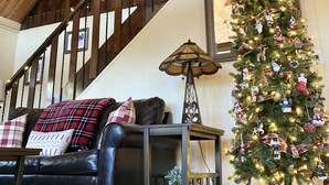 A cozy living room with a wooden staircase, a black leather sofa, a Christmas tree, and a lamp. - Spacious Prescott Forest Cabin, Game Room, 15 minutes to Downtown Prescott (Prescott)