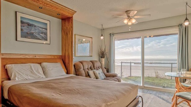 A bedroom with a large bed, a chair, a table, and a view of the ocean.