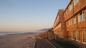 A beachfront hotel with a wooden facade, a walkway leading to the beach, and a view of the ocean.