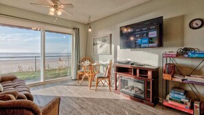 A spacious living room with a large TV, a fireplace, and a view of the ocean.
