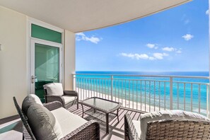 Un balcón con mobiliario de mimbre y una puerta de cristal, con vistas a una playa de aguas azules y transparentes.