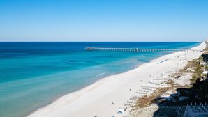 A beach with a long pier extending into the ocean, a sandy shoreline, and a clear blue sky.