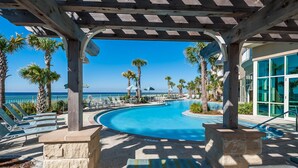 A pool area with lounge chairs and palm trees, overlooking a clear blue sky and ocean.