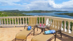 A balcony with a table and chairs, overlooking a scenic view of a lake and hills.