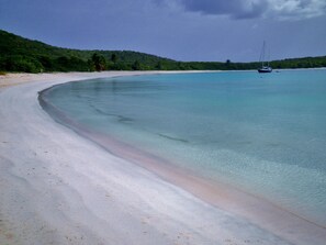 Una platja amb aigua turquesa cristal·lina, sorra daurada i un veler a la distància.
