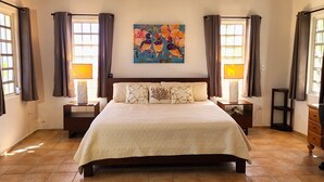 A hotel room with a large bed, two bedside tables, a painting on the wall, and curtains on the windows.