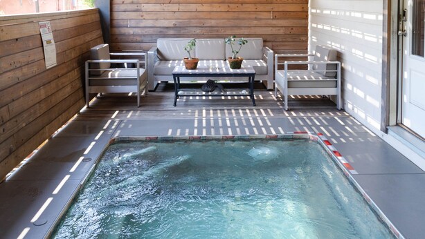 A covered pool area with a wooden ceiling, seating, and a small table with a plant. - Porch House W/Swim Spa/Pool &3 Big Screens To Enjoy  (New Orleans)