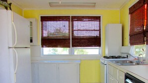 A compact kitchen with white cabinets, a refrigerator, a stove, and a sink. - Direct Oceanfront Cottage-Sunrise View- #2, (Little Torch Key)