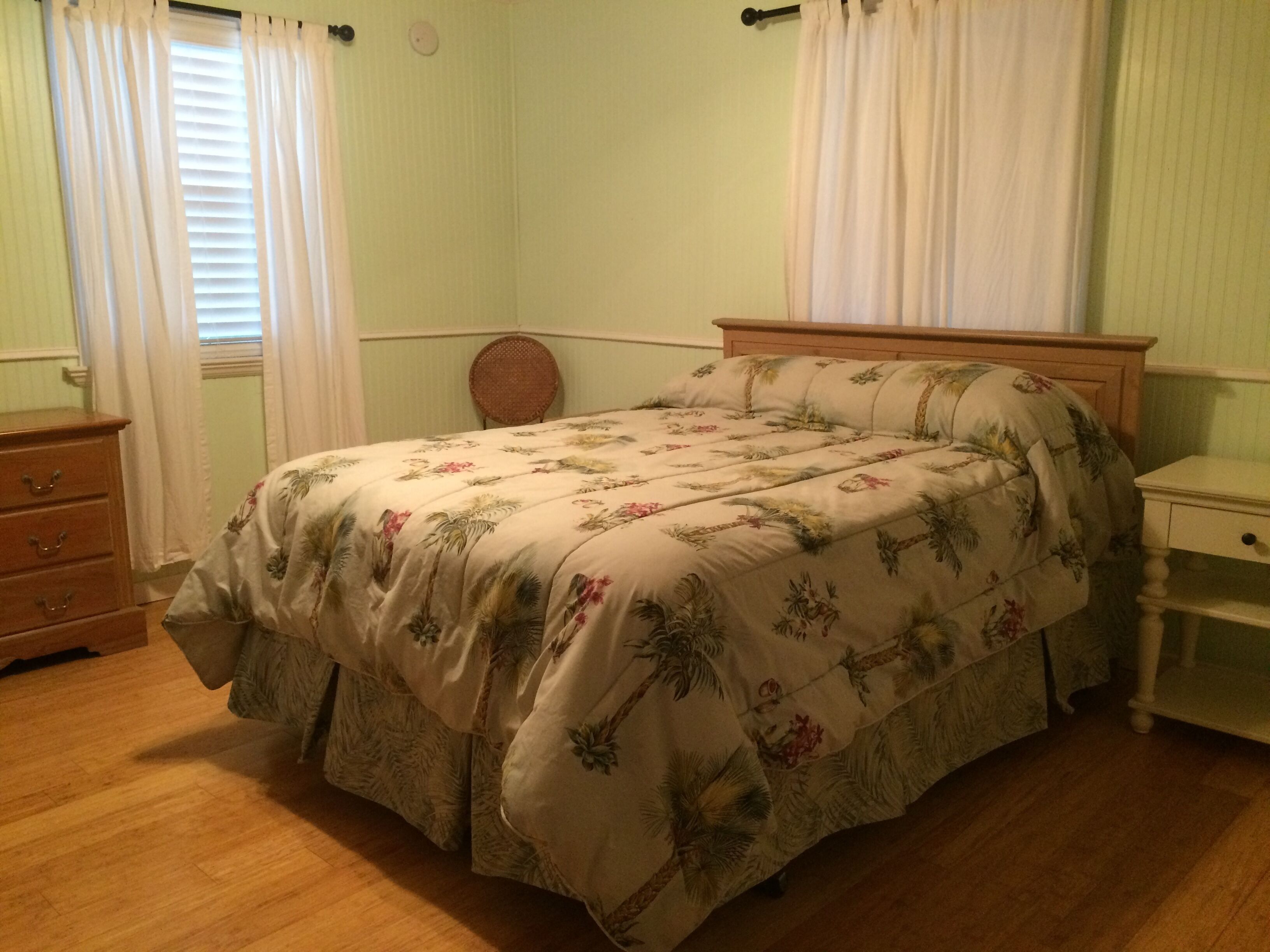 Une chambre à coucher avec un lit, une commode, une table de chevet et une fenêtre avec des rideaux.