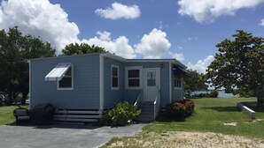A small, single-story blue mobile home with a front porch, a covered patio, and a lawn. - Direct Oceanfront Cottage-Sunrise View- #2, (Little Torch Key)
